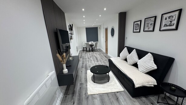 A modern living room with a black sofa, a round coffee table, and a dining area in the background. - Apartmentsleeps6-familly&petfriendly (Manchester)