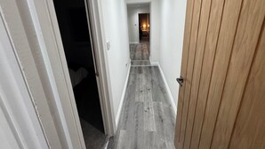 A hallway with a wooden door on the right, a white door on the left, and a light fixture on the ceiling. - Apartmentsleeps6-familly&petfriendly (Manchester)