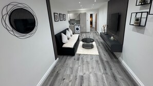 A modern living room with a sofa, coffee table, and TV. There is a kitchen in the background with a washing machine. - Apartmentsleeps6-familly&petfriendly (Manchester)
