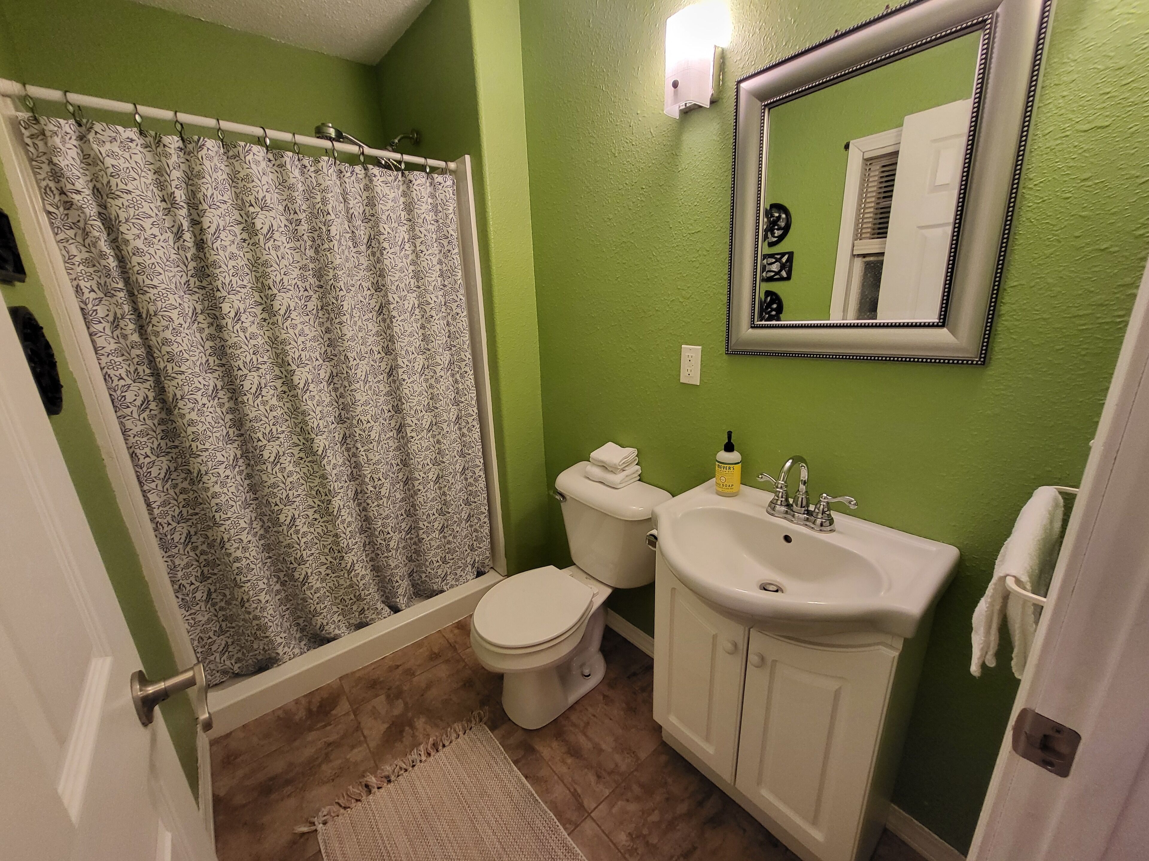 A bathroom with a shower curtain, toilet, sink, and mirror.