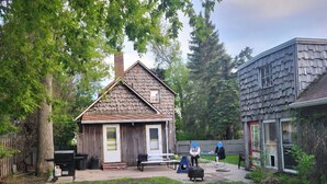 A wooden house with a chimney, a fenced yard, and a dog running.