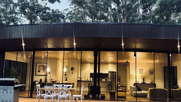 Une maison moderne avec une façade en verre, un espace salon extérieur et une terrasse en bois.