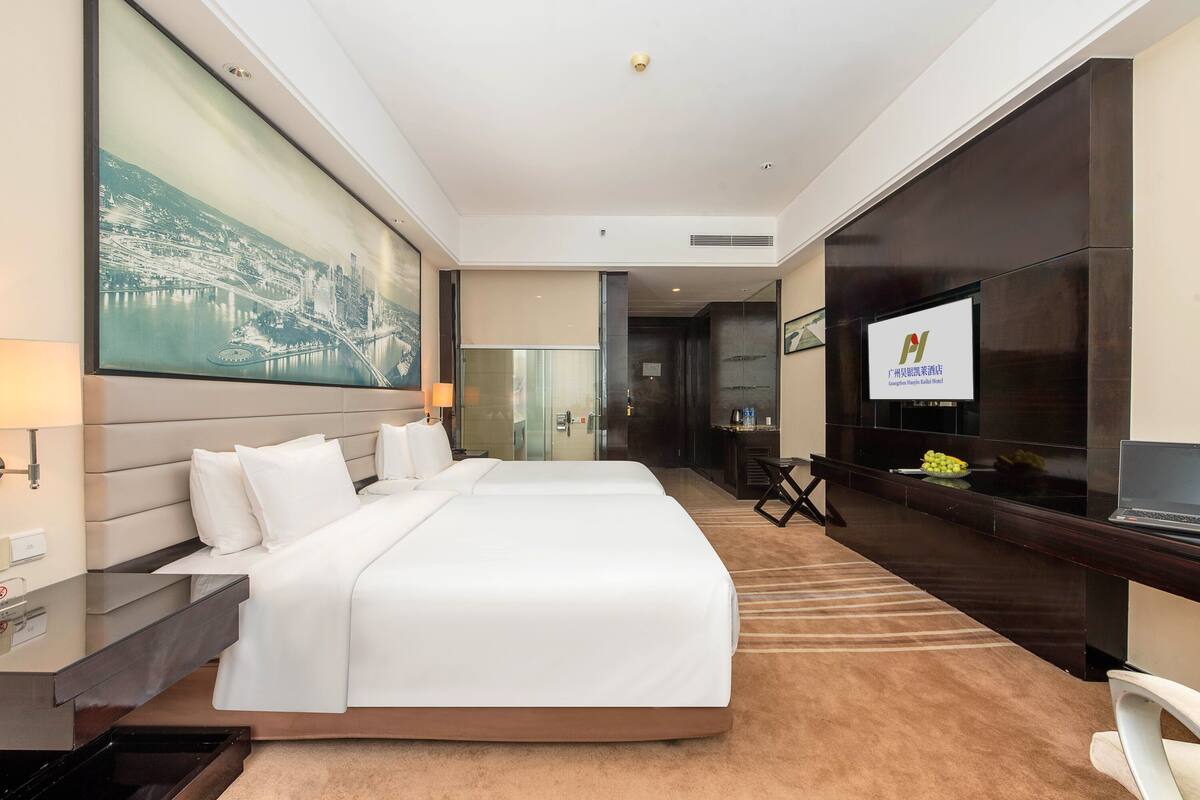 A hotel room with a large bed, a desk with a computer, a TV, and a large painting on the wall.