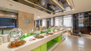Zona de bufé con varias estaciones de comida, área de cocina y zona de estar con mesa y sillas.