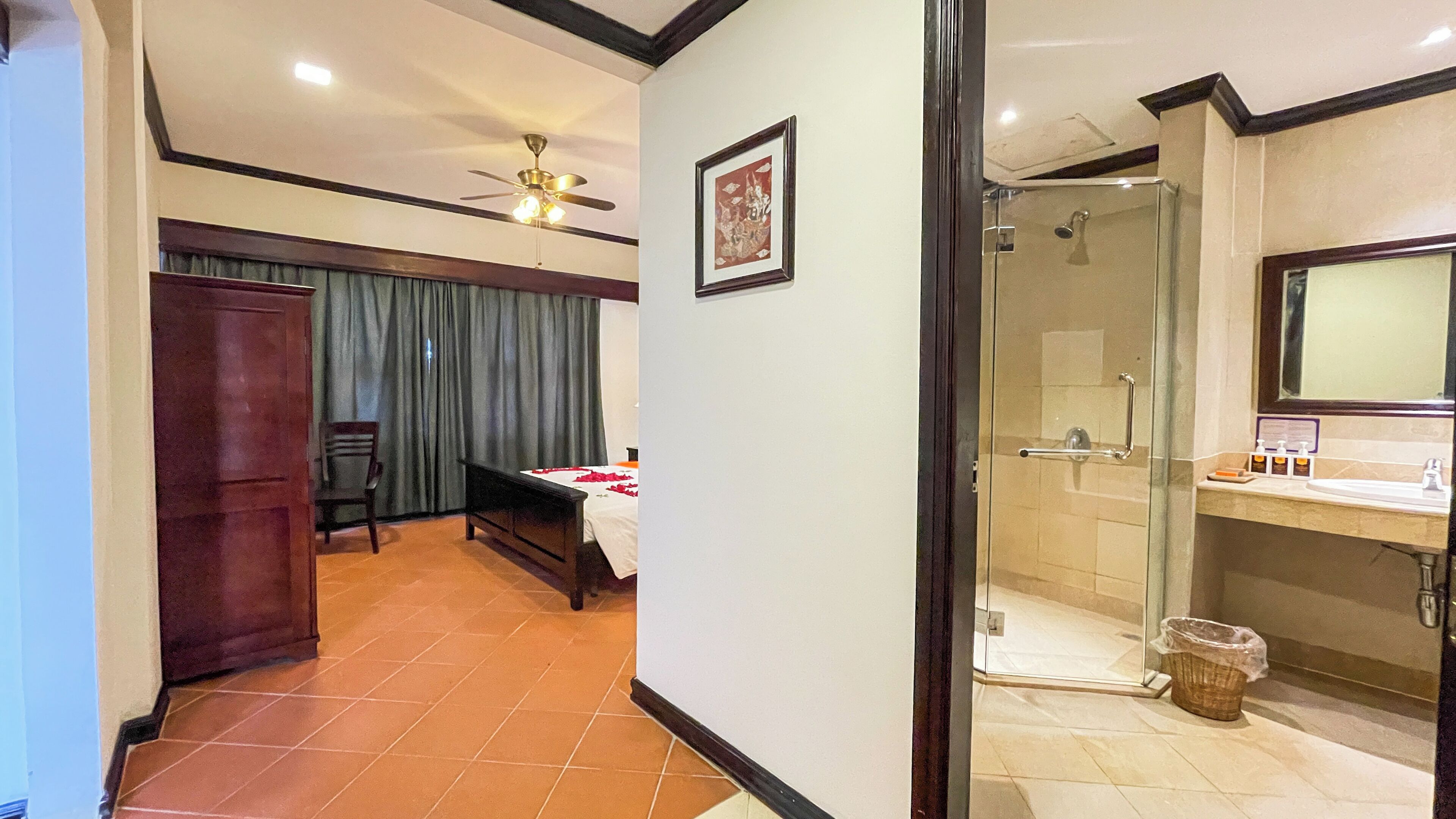 A hotel room with a bed, a desk, a chair, a wardrobe, a shower, and a bathroom with a sink and mirror.