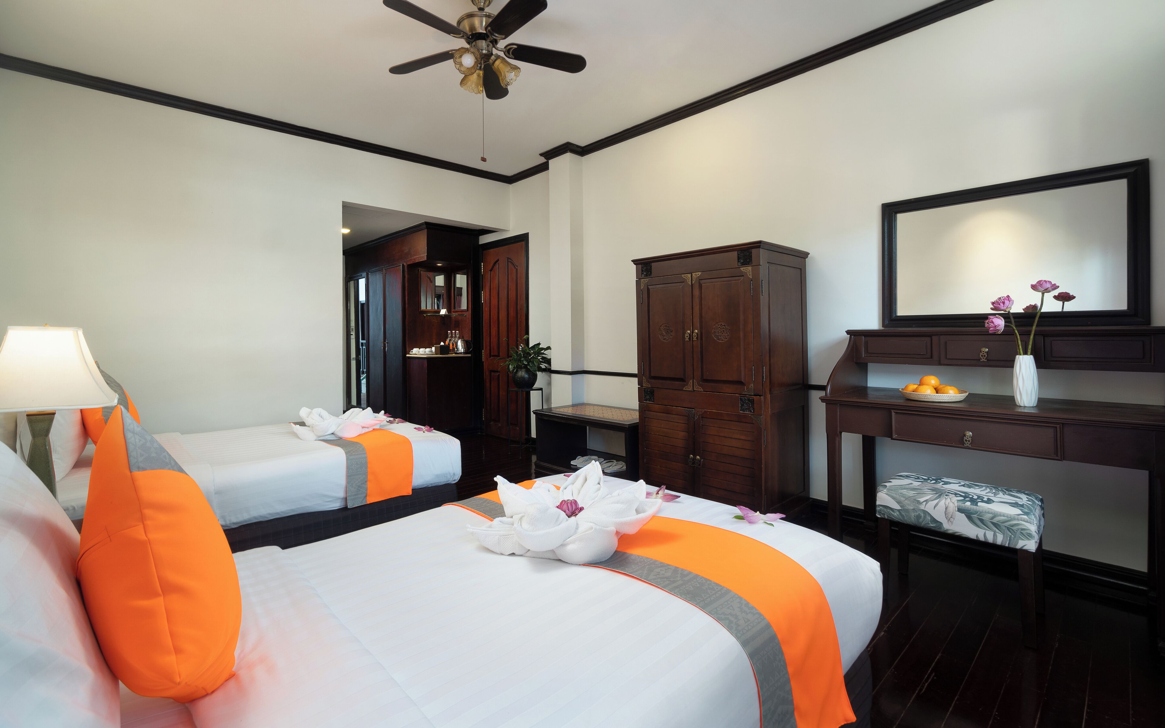 Quarto de hotel com duas camas, uma escrivaninha, um guarda-roupa e um ventilador de teto.