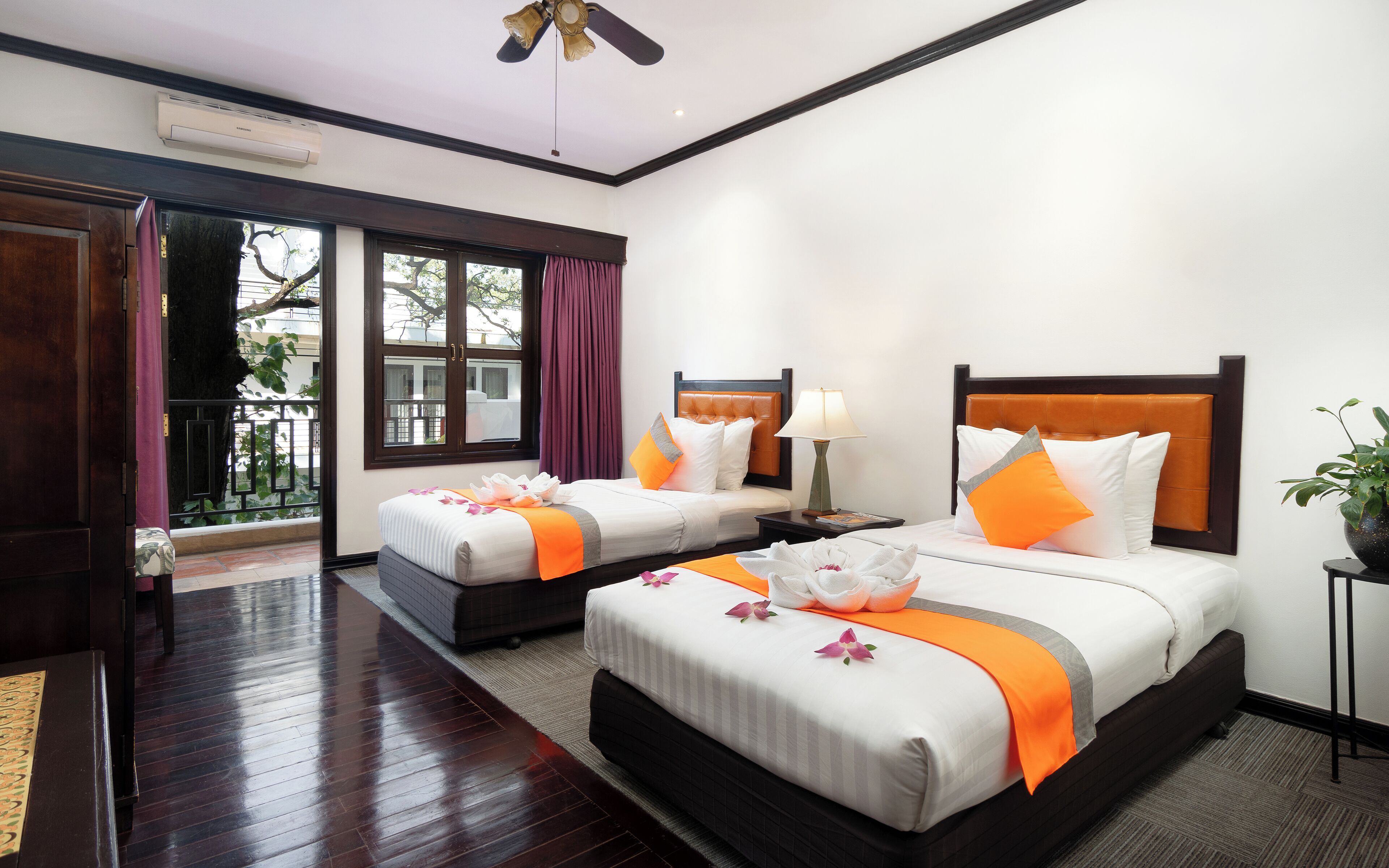 A hotel room with two beds, a window with curtains, a ceiling fan, and a potted plant.