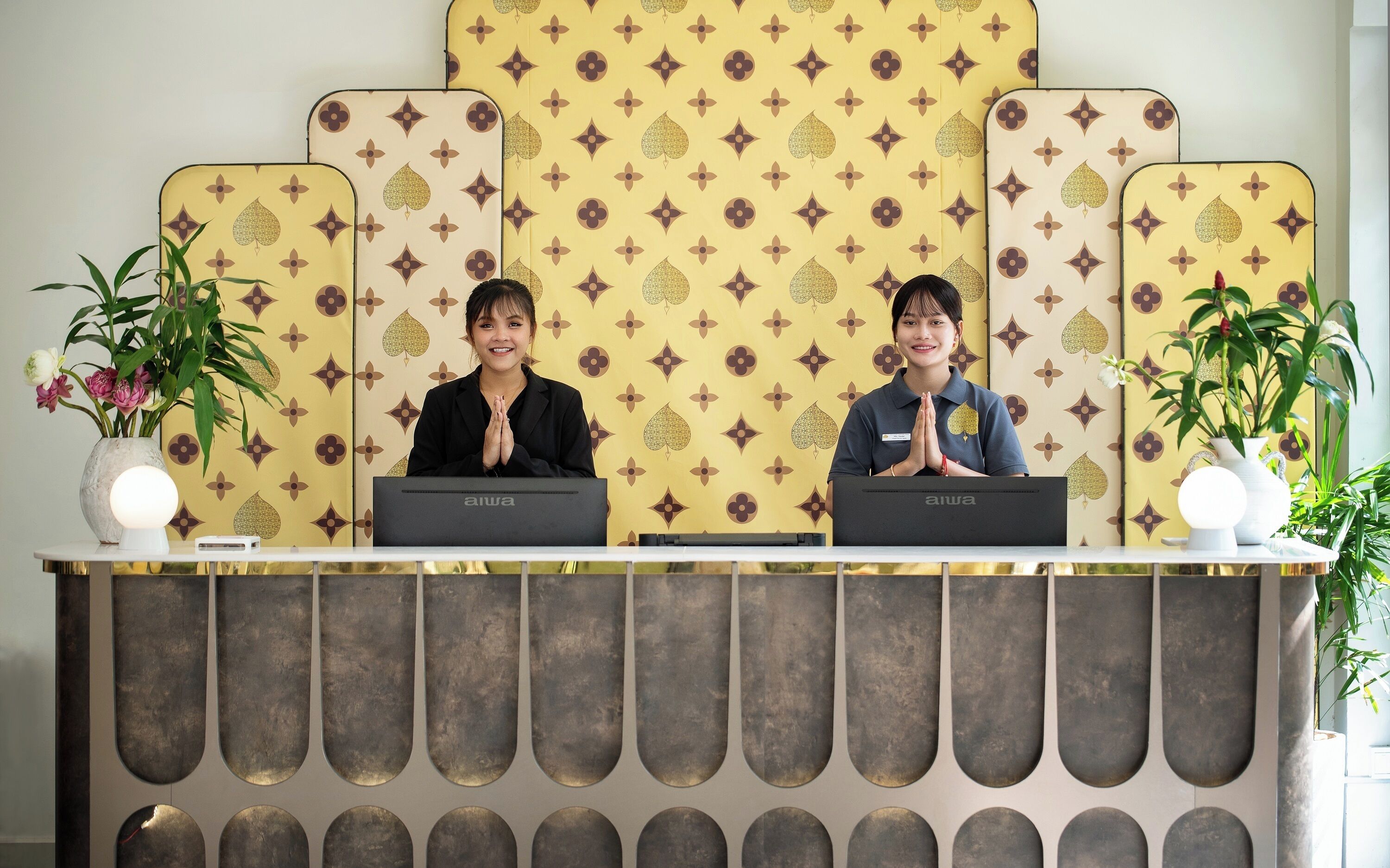 Un mostrador de recepción con un fondo estampado con el diseño de Louis Vuitton, dos empleados detrás y plantas en macetas a ambos lados.