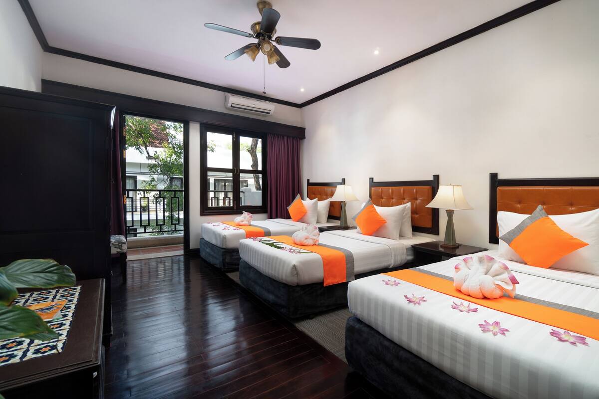 Habitación de hotel con tres camas, ventilador de techo, aire acondicionado y vista al exterior.
