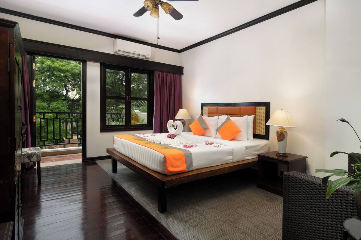 Habitación de hotel con una cama grande, una mesita de noche con lámpara, una planta en maceta y vistas a zonas verdes.