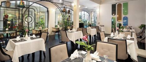 A restaurant with multiple tables set for dining, featuring white tablecloths and neatly arranged cutlery.