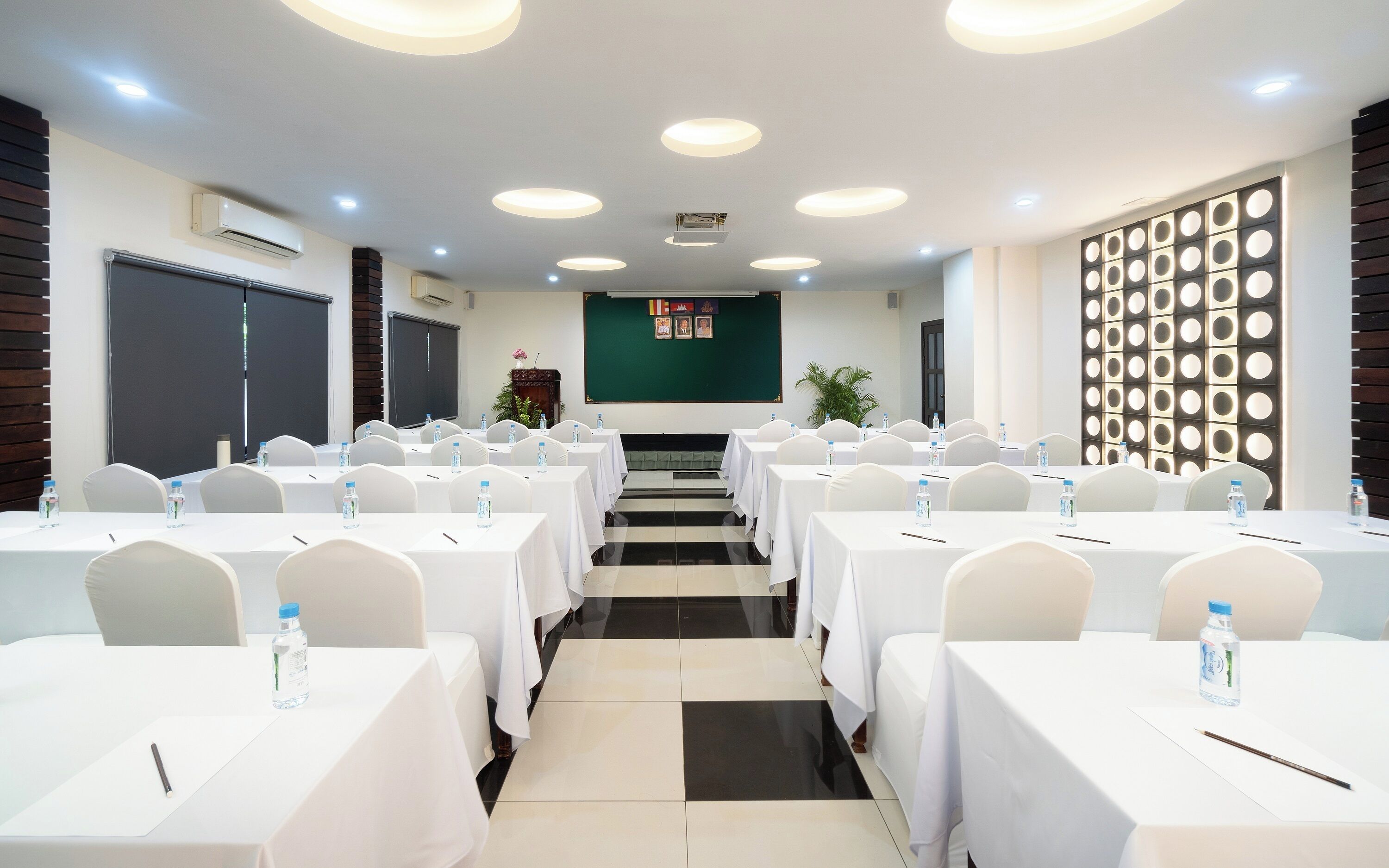 Un salón de conferencias con varias mesas y sillas, una pantalla verde y una pared decorativa con patrones circulares.