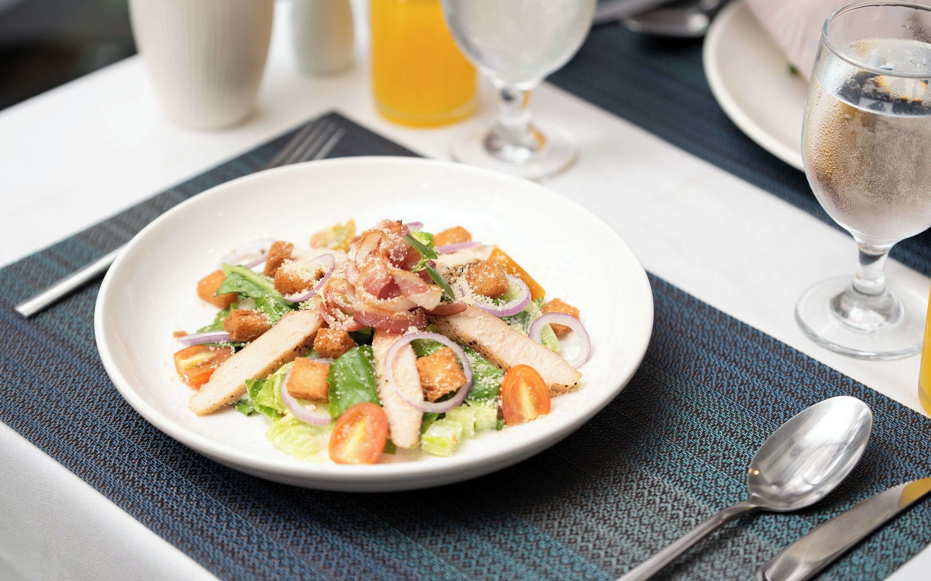 A plate of salad with croutons, bacon, and cheese on a table with a napkin, fork, and spoon.