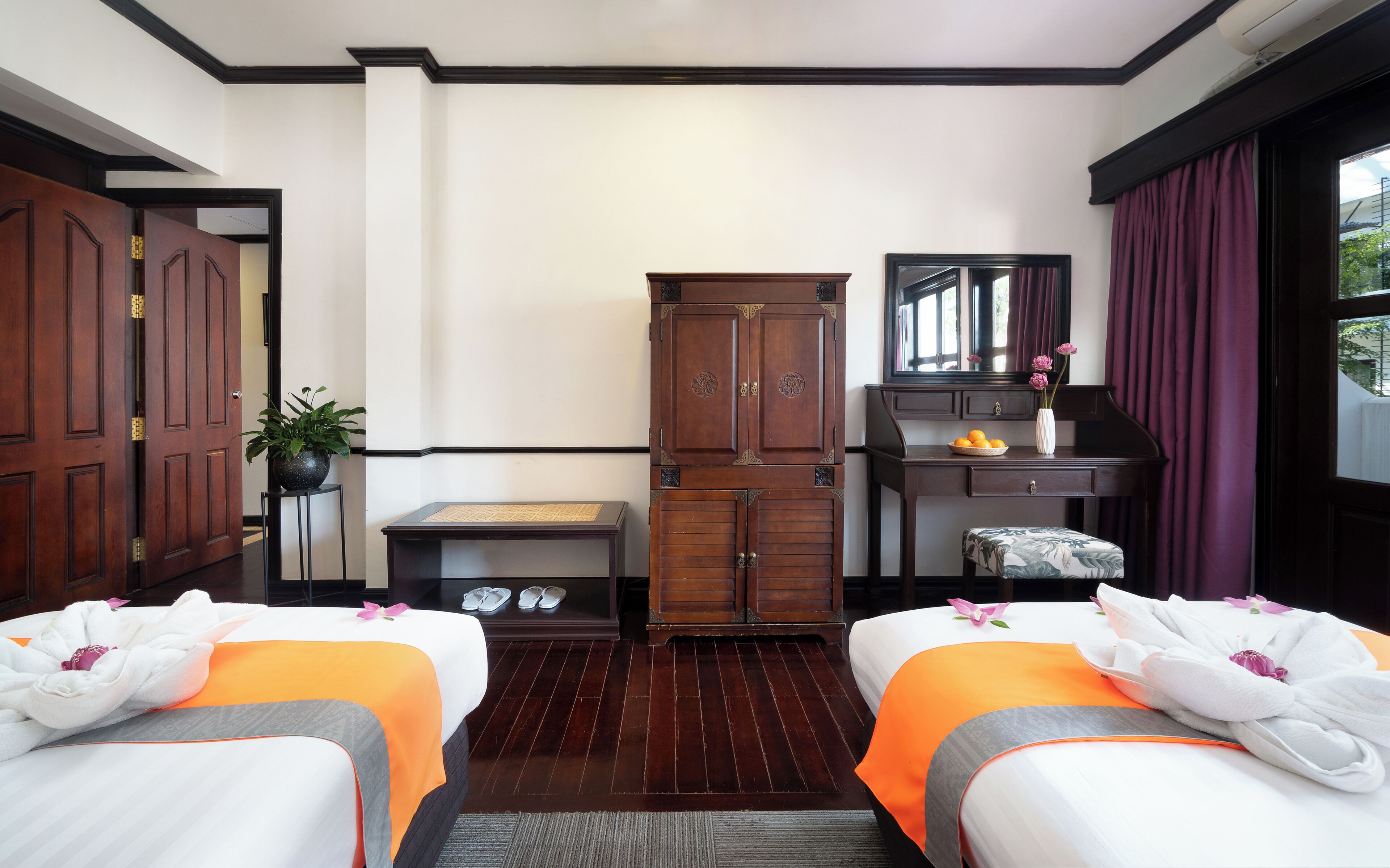 Una habitación de hotel con dos camas, un armario de madera, un escritorio con espejo y una ventana con cortinas.