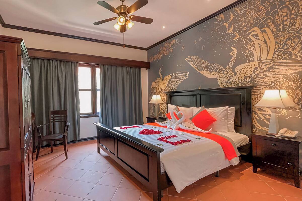 Una habitación de hotel con cama, una silla, un escritorio y un ventilador de techo.