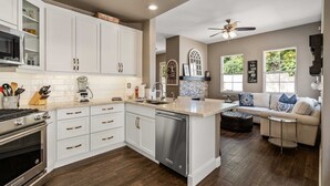 A modern kitchen with white cabinetry, a built-in oven, and a dishwasher. There is a dining area with a white sofa and a coffee table. - Charming 3-bedroom furnished, home with WiFi, AC in Spanish Hills Camarillo (Camarillo)