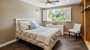 A bedroom with a bed, a nightstand, a chair, a window, and a ceiling fan. - Charming 3-bedroom furnished, home with WiFi, AC in Spanish Hills Camarillo (Camarillo)