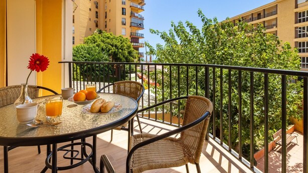 A balcony with wicker furniture, a table with a glass of orange juice, and a red flower. - Torre Copenhague - Terrace, Swimming Pool, Bechfront (Torremolinos)