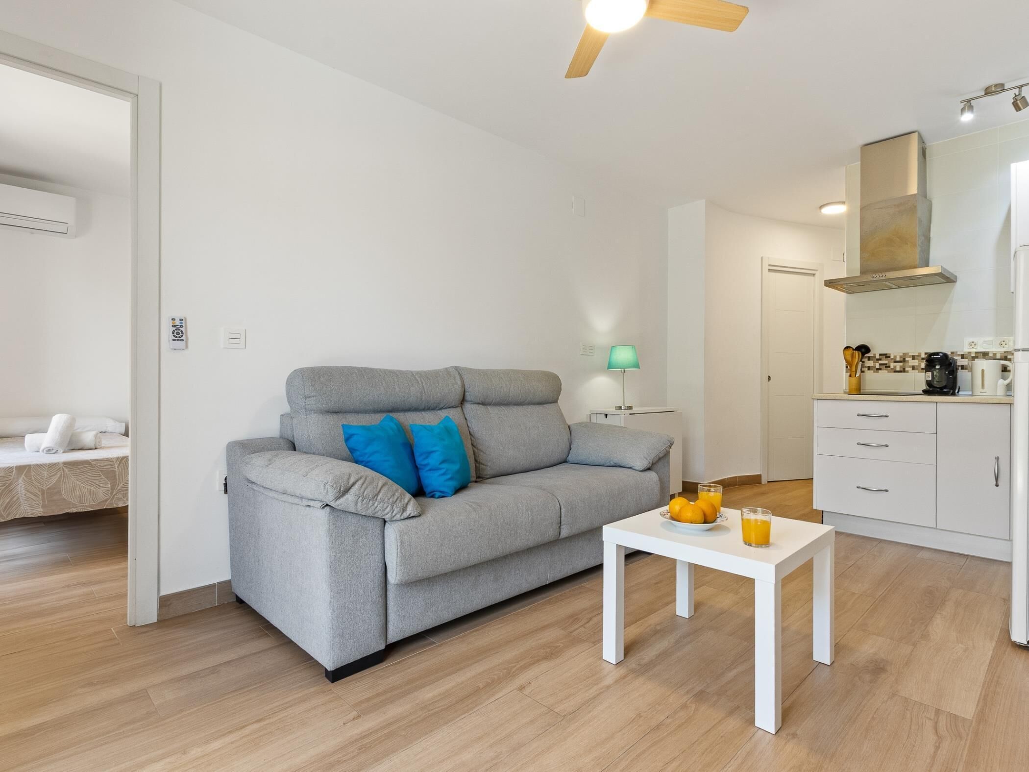 Una sala de estar moderna con un sofá gris, una mesita blanca y una cocina con armarios blancos y una estufa.