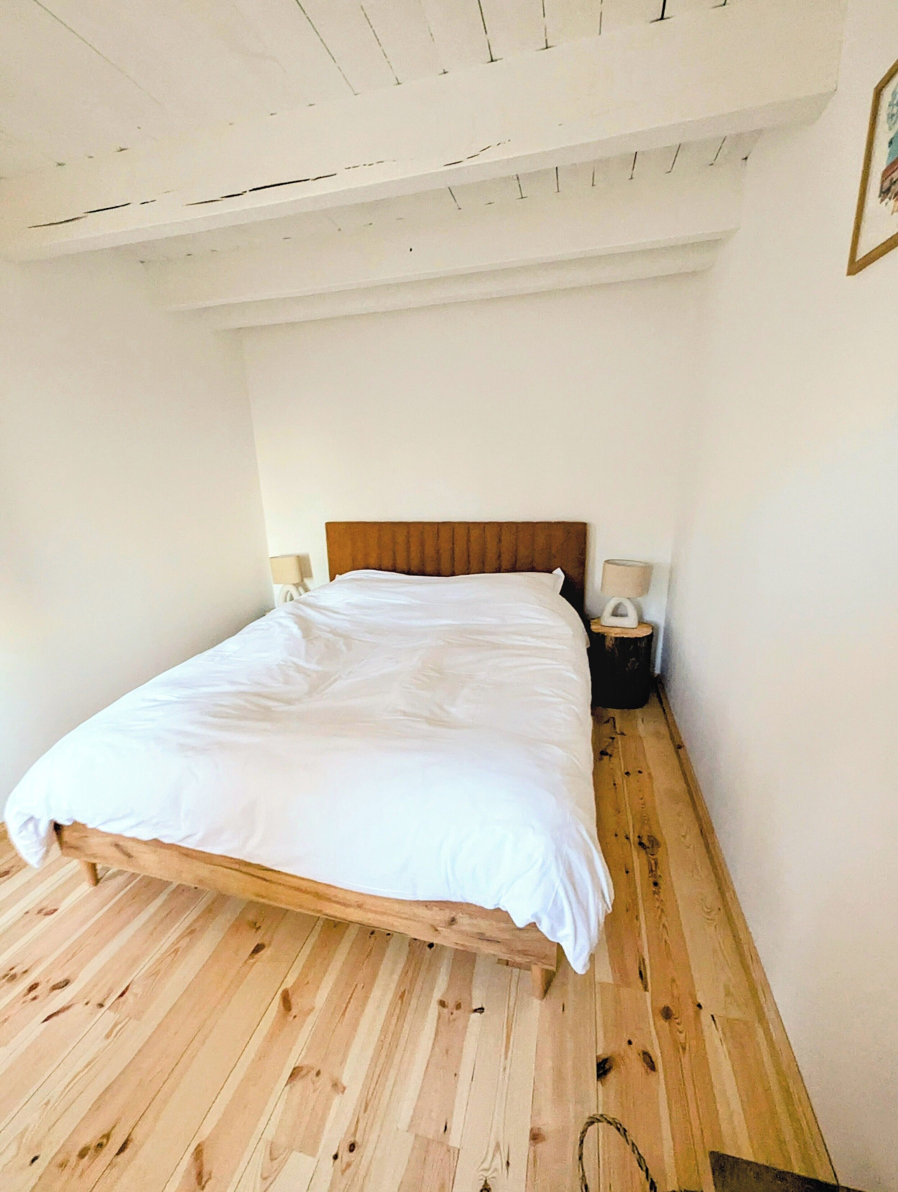 A single bed with a wooden headboard in a room with wooden flooring and white walls.