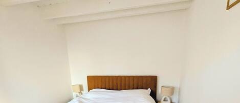 A single bed with a wooden headboard in a room with wooden flooring and white walls.