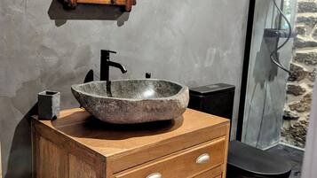 Un baño con tocador de madera, lavamanos de piedra, espejo y zona de ducha.