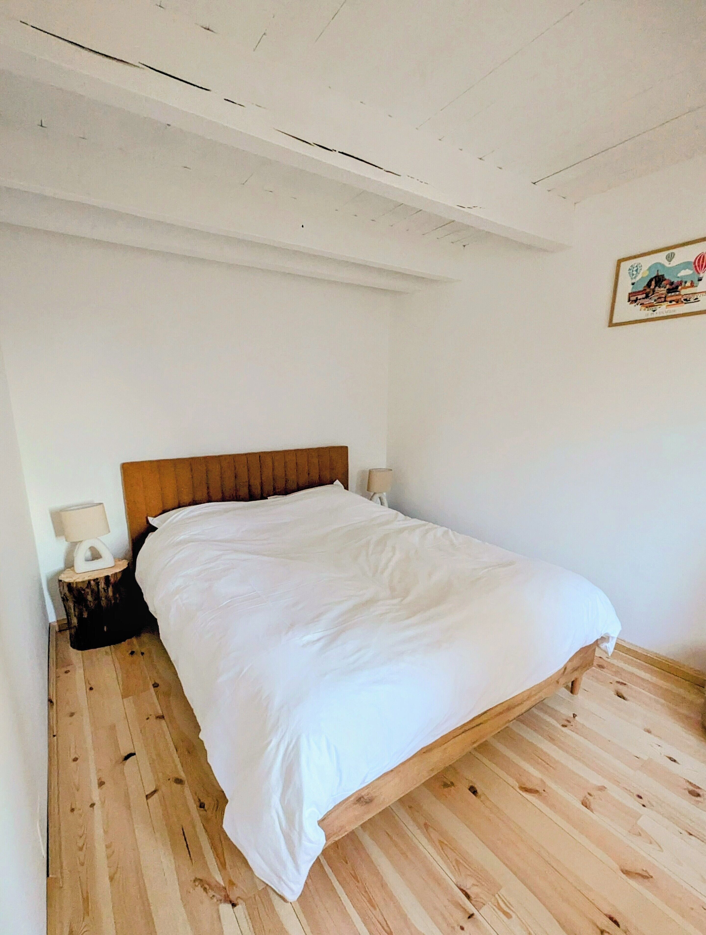 A bedroom with a wooden bed, a nightstand with a lamp, and a wall-mounted picture.