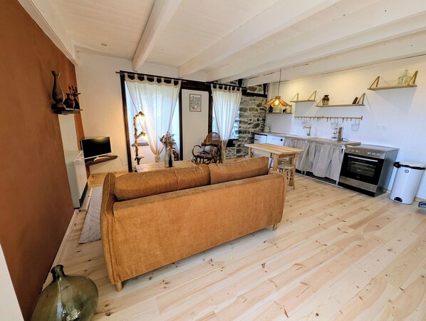 A cozy living room with a sofa, a television, and a kitchen area with a stove and shelves.