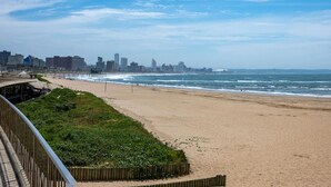 A beach with a city skyline in the background, a wooden boardwalk, and a sandy shore.