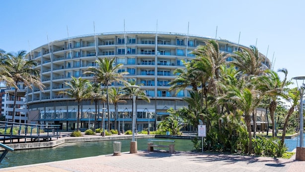 A multi-story hotel with balconies, a pool area, and palm trees.