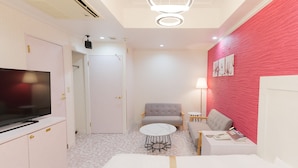 Habitación de hotel con televisor, cama, sofá, una mesita redonda y una pared de acento roja.
