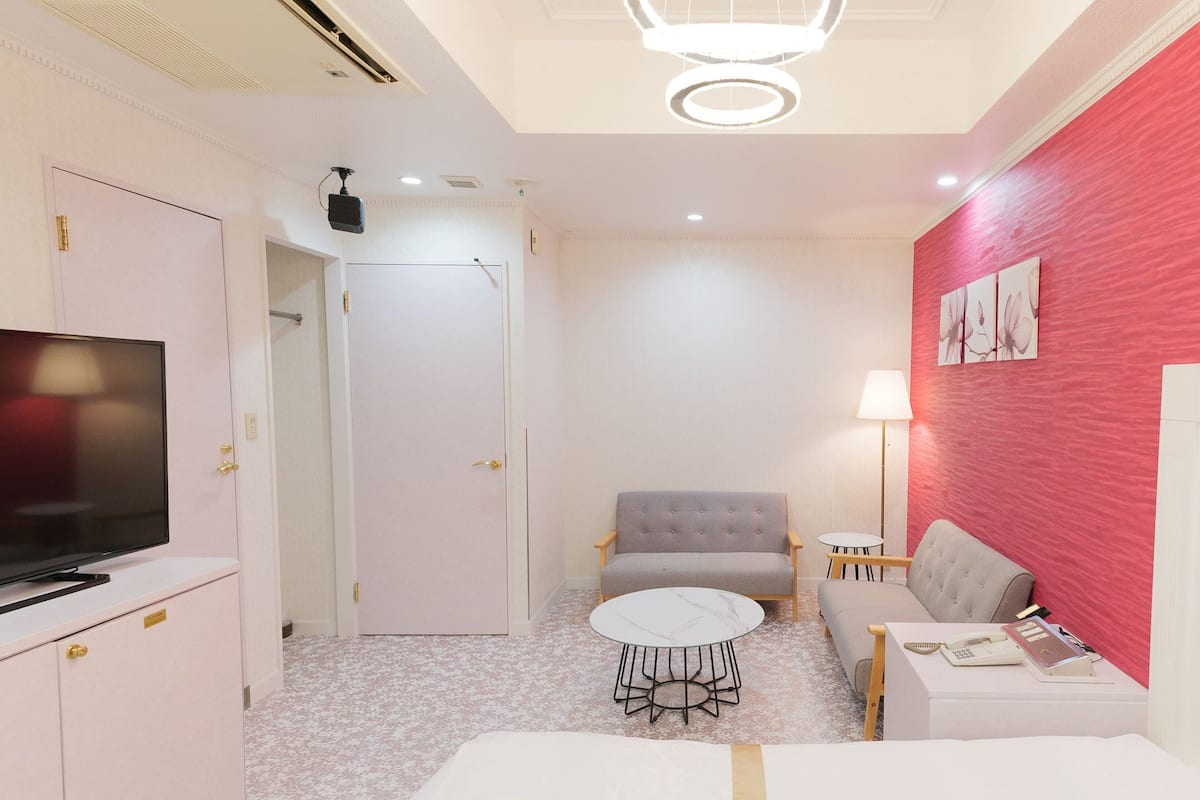 A hotel room with a television, a bed, a sofa, a small round table, and a red accent wall.