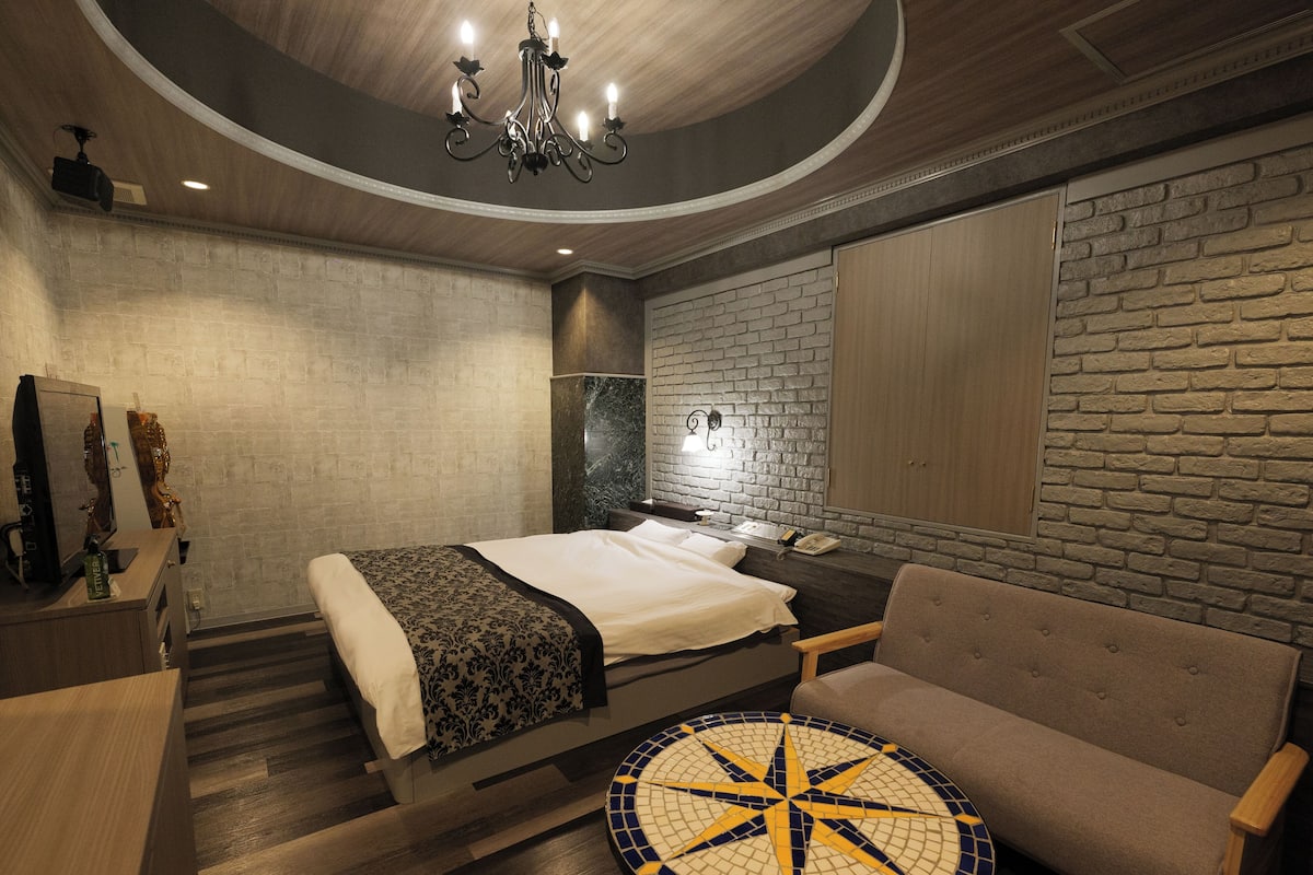 A modern hotel room with a bed, a round table, a sofa, and a brick wall.