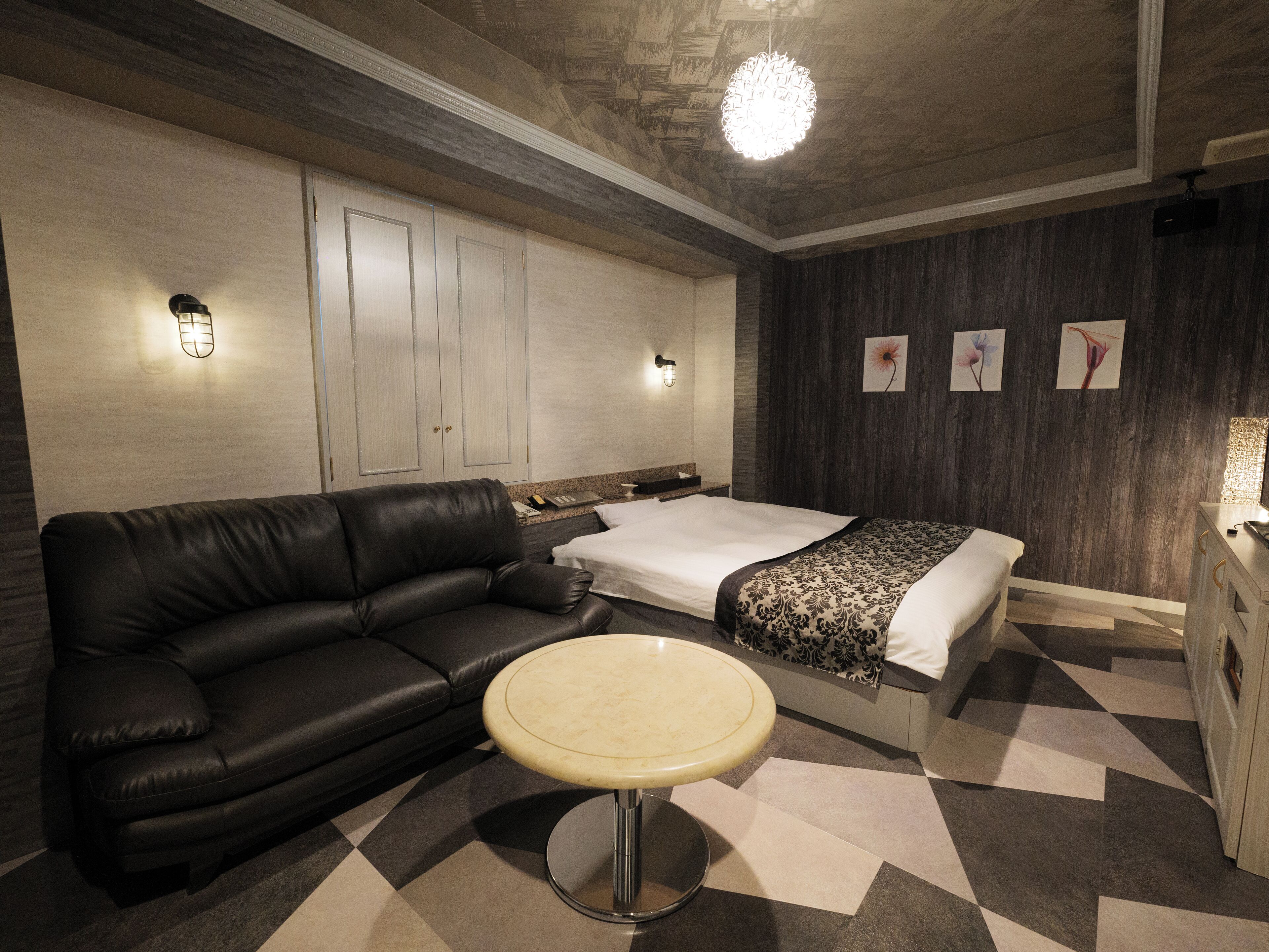 A hotel room with a black leather sofa, a round table, a bed with a patterned bedspread, and a wall with framed artwork.