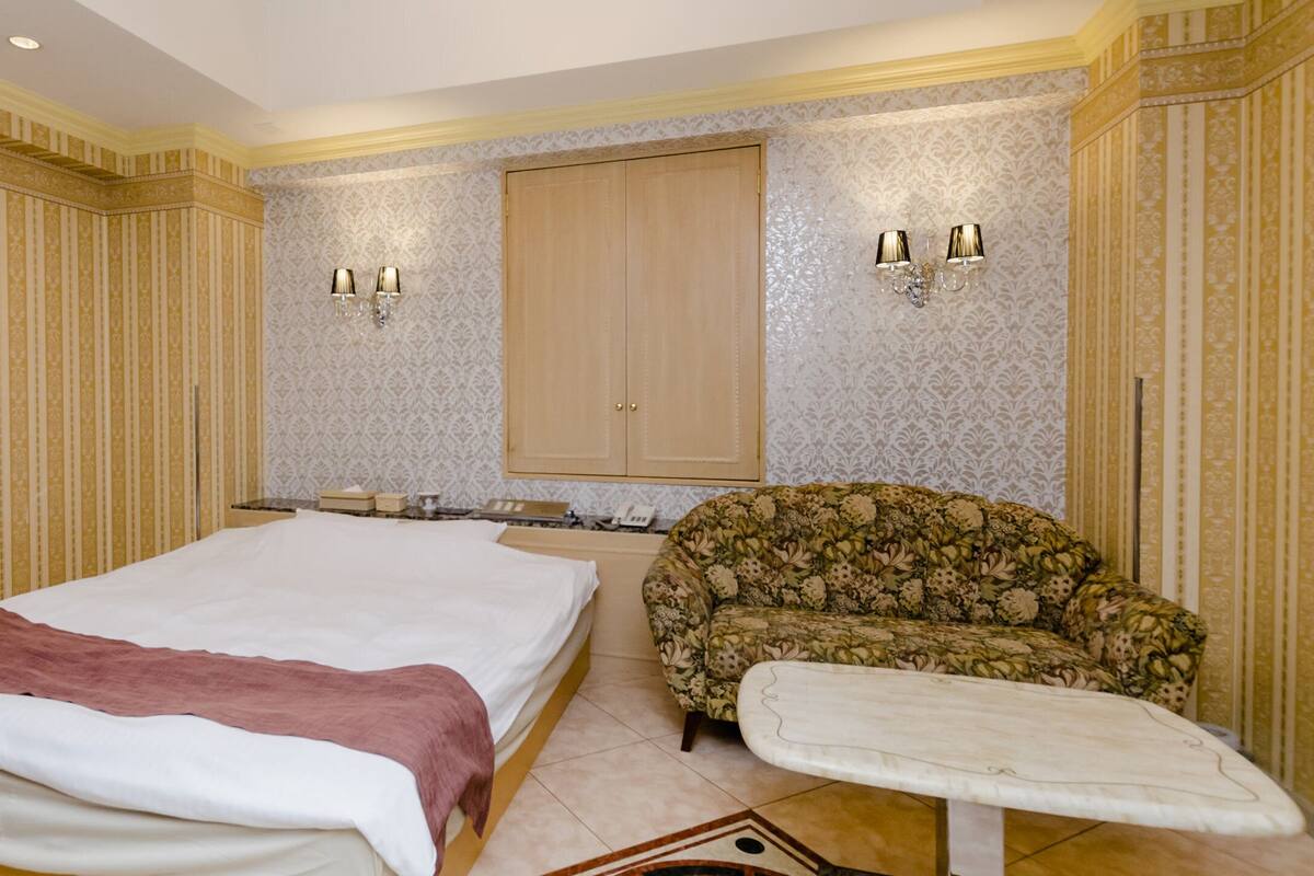 A hotel room with a large bed, a sofa, a small table, and two wall-mounted lamps.