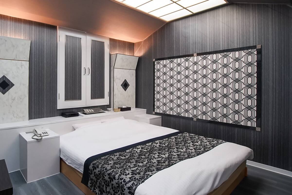 A modern hotel room with a large bed, a desk with a phone, a chair, and a patterned wall decoration.