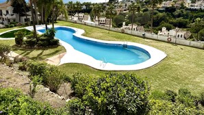 Une piscine au design incurvé, entourée de pelouse bien entretenue et de palmiers.