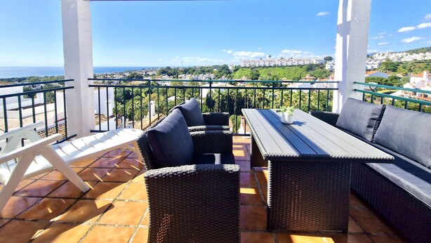 Une terrasse dotée de meubles en osier, d’une table et offrant une vue sur la ville et la mer.