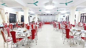 A large banquet hall with round tables and red chairs, white pillars, and ceiling fans. - SVFU Ha Noi (Hanoi)