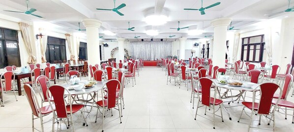 A large banquet hall with round tables and red chairs, white pillars, and ceiling fans. - SVFU Ha Noi (Hanoi)