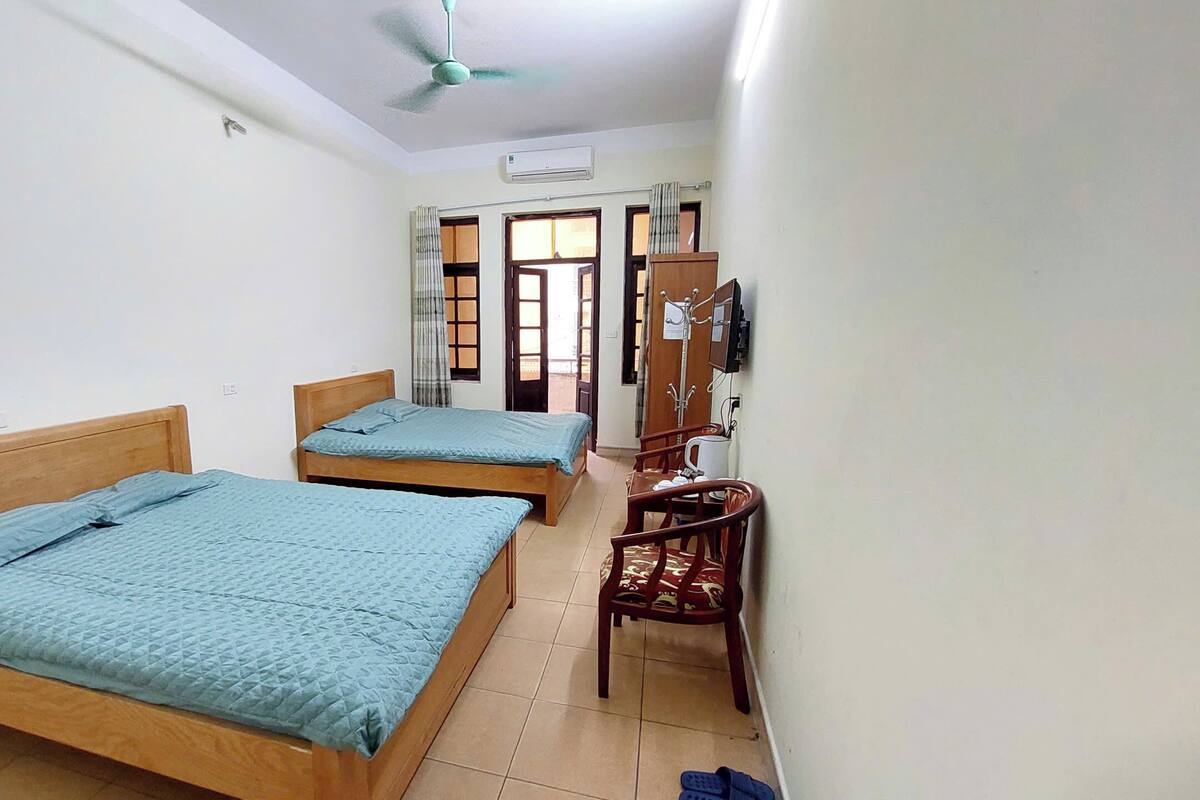 A room with two wooden beds, a ceiling fan, an air conditioning unit, a wooden chair, and a television.