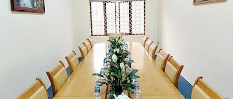 Un salón de conferencias con una larga mesa, sillas, un ventilador de techo y obras de arte en las paredes.