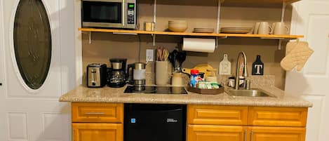 A compact kitchen with a built-in dishwasher, a microwave, and a coffee maker. There are wooden cabinets and a countertop with various kitchen items.