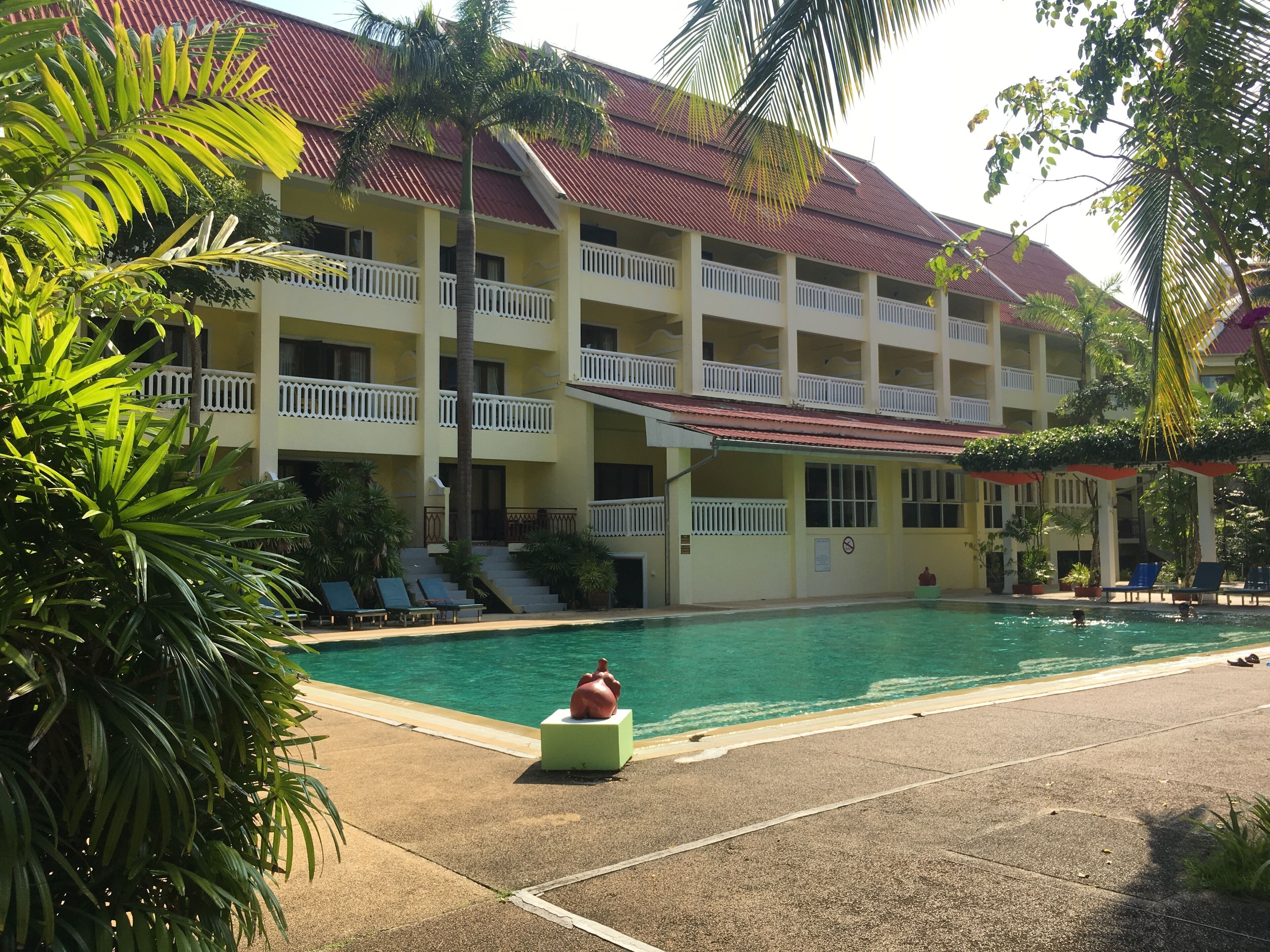 Et hotel med swimmingpool, flere balkoner og palmer.
