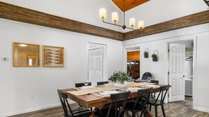 A dining area with a wooden table set for six, surrounded by black chairs. There are two framed artworks on the wall, a ceiling light fixture, and a door leading to another room. - Lake Front ~ Firepit ~ Kayaks ~ SUPs ~ Yard Games - Holiday Home (Gaylord)