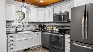 A modern kitchen with white cabinets, stainless steel appliances, and a wooden ceiling. - Lake Front ~ Firepit ~ Kayaks ~ SUPs ~ Yard Games - Holiday Home (Gaylord)