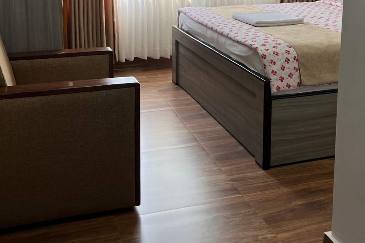 Une chambre à coucher comprenant un lit, une chaise, un appareil de climatisation et une fenêtre avec des rideaux.