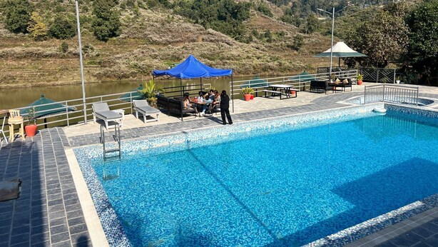 Ein Schwimmbecken mit gefliestem Deck, einer blauen Markise und Gartenmöbeln.