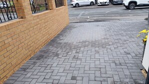 Ein gepflasterter Weg mit einer Backsteinmauer an einer Seite und einer Straße mit Autos im Hintergrund.