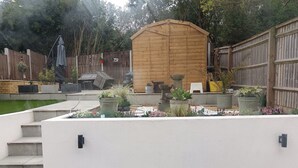 Ein Garten mit einem Holler Schuppen, Betonstufen und verschiedenen Kübelpflanzen.